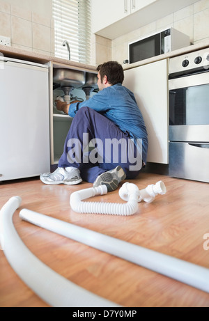 Plumber working on pipes under sink Stock Photo