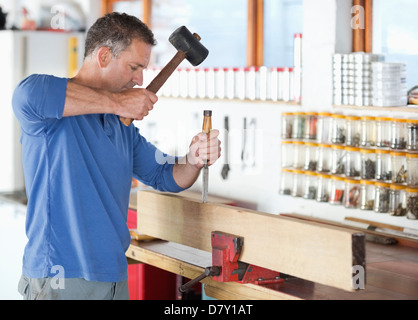 Side view of serious middle aged carpenter using spray gun for painting  wood detail with white