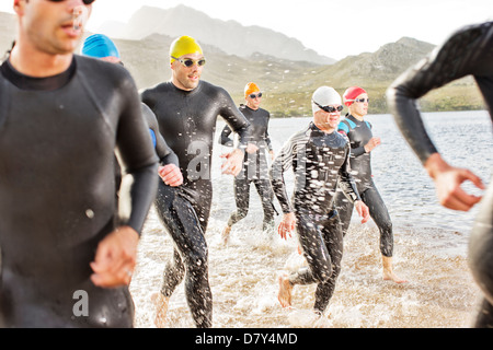 Triathletes in wetsuits walking in waves Stock Photo