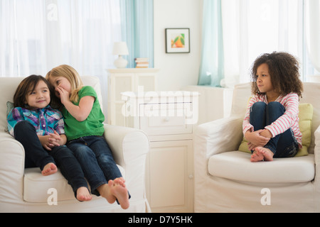 Girls whispering away from friend in living room Stock Photo