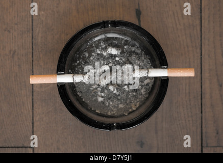 Two cigarettes in an ash tray on wooden table Stock Photo
