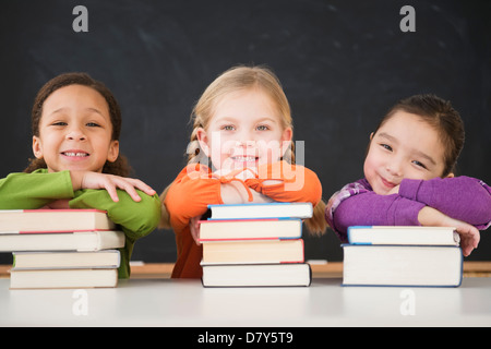 Girls leaning on stacks of books in classroom Stock Photo