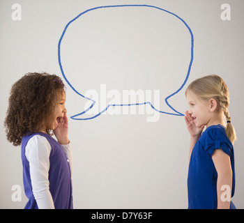 Girls whispering with empty speech bubble Stock Photo