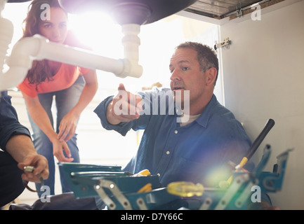 Plumbers working on pipes under sink Stock Photo