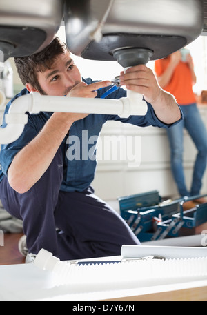 Plumber working on pipes under sink Stock Photo