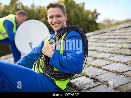 Workers installing satellite dish on roof Stock Photo