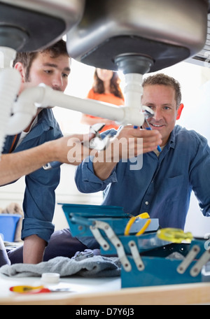 Plumbers working on pipes under kitchen sink Stock Photo