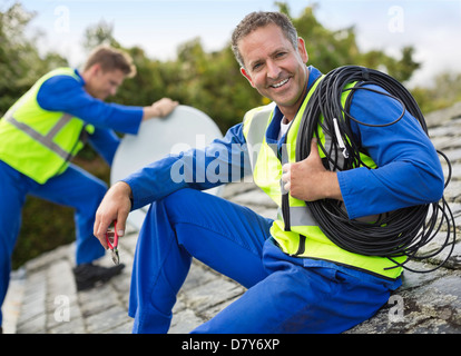 Workers installing satellite dish on roof Stock Photo
