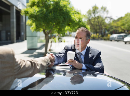 Businessmen shaking hands over car Stock Photo
