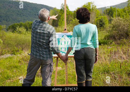 Caucasian couple visualizing house in rural landscape Stock Photo