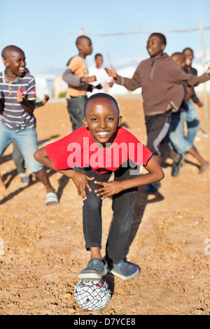 Boys playing soccer together in dirt field Stock Photo