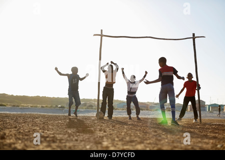 Boys playing soccer together in dirt field Stock Photo