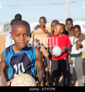 Boys holding soccer balls in dirt field Stock Photo