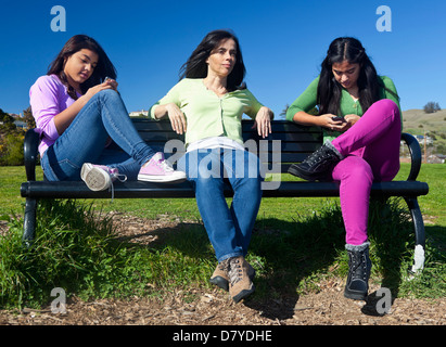 Hispanic mother and daughters sitting on park bench Stock Photo