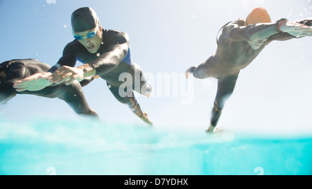 Triathletes in wetsuits running into ocean Stock Photo