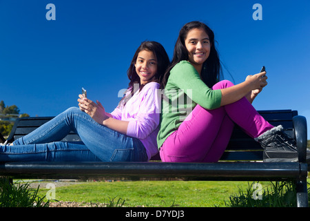 Hispanic teenage girls sitting on park bench Stock Photo