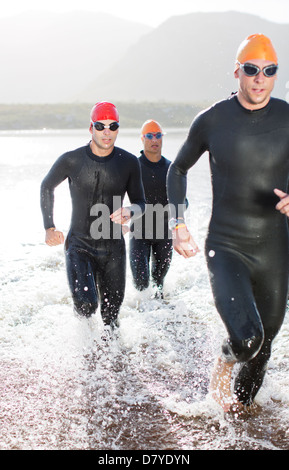 Triathletes in wetsuits running in waves Stock Photo