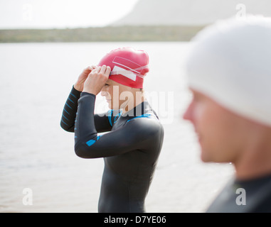 Triathletes pulling on goggles on beach Stock Photo
