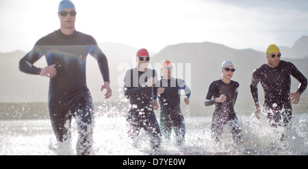 Triathletes in wetsuits running in waves Stock Photo