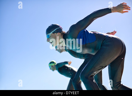 Triathletes diving into water outdoors Stock Photo