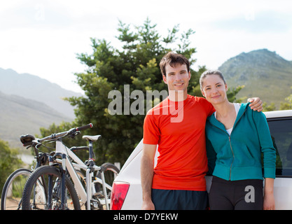 Couple smiling by car in rural landscape Stock Photo