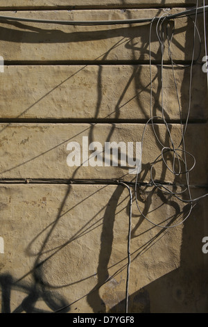 electricity power wiring circuit cables tubes on side of property wall in sun Stock Photo