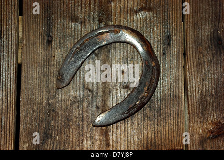 Old rusted horseshoe hanging on stable wooden door. Stock Photo