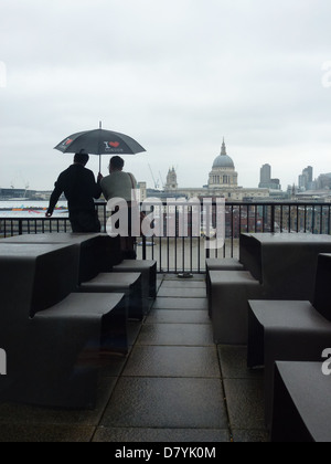 Couple with I love London umbrella overlooking London and St Paul's from the balcony of the Tate Modern on a rainy day, Stock Photo