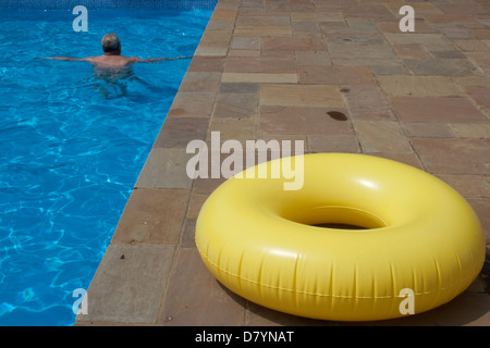 Man swimming in pool with yellow ring on the side Stock Photo