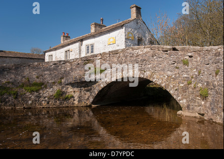Historic stone single-span bridge over water of Malham Beck in centre of scenic Dales village in sunny summer - Malham, North Yorkshire, England, UK.