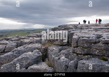 People standing & walking on upland limestone pavement, spectacular natural feature at top of Malham Cove - Malhamdale, Yorkshire Dales, England, UK. Stock Photo