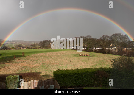 Beautiful rainbow creating a perfect arch across rain clouds in sky, over sunlit fields in rural landscape - Baildon, West Yorkshire, England, UK. Stock Photo