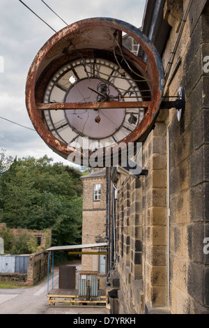 Close-up of large broken rusty clock fixed to wall at Greenholme Mills, a partially derelict Victorian worsted mill - near Ilkley, Yorkshire, England. Stock Photo