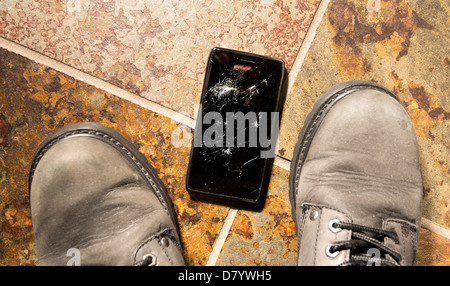 A smartphone lies broken between the workboots of its owner just after being dropped. Stock Photo