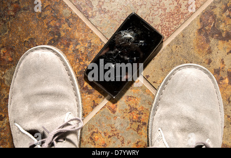 A smartphone lies broken between the shoes of its owner just after being dropped. Stock Photo