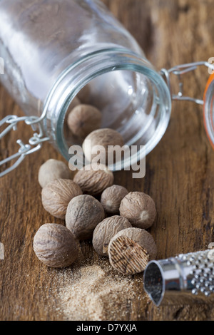 Many nutmegs are an empty spice jar on a rustic wooden background Stock Photo