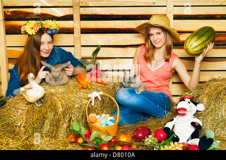 two girl with rabbit, cat and harvest on hayloft at summer day Stock Photo