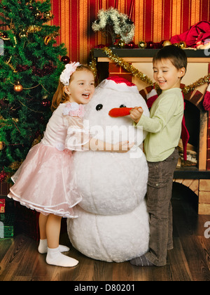 two beautiful child and toy snowman near christmas tree Stock Photo