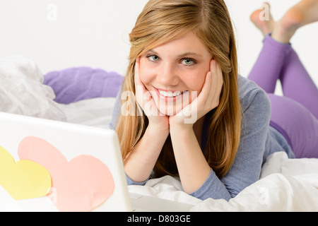 Young smiling girl lying on bed with laptop Stock Photo