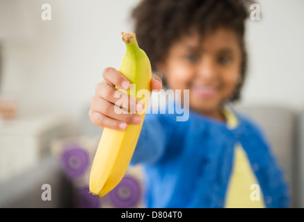 African American girl holding banana on sofa Stock Photo