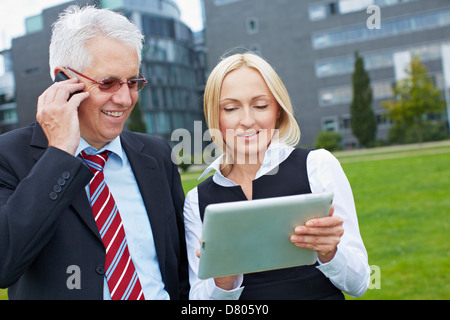 Two business people with smartphone and tablet PC outdoors Stock Photo