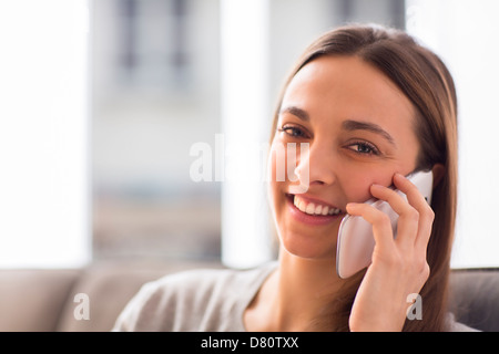 Pretty young woman using white smart phone at home looking at the camera Stock Photo