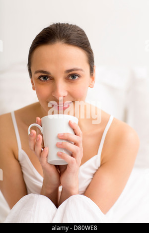 Portrait female enjoying tea in white bedroom Stock Photo