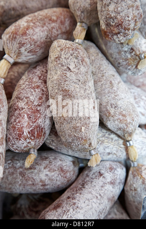 A cured salami with a white mold coating and a red string tie rests on ...