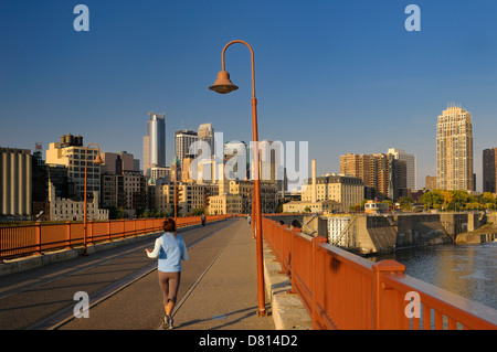 Early morning jogger and Minneapolis highrise towers skyline and Lock and Dam 1 from the Stone Arch Bridge at sunrise Minnesota USA Stock Photo