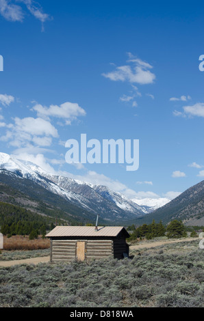 An old abandoned log cabin is situated with a stunning view of the snow capped Rocky Mountains of Colorado. Stock Photo