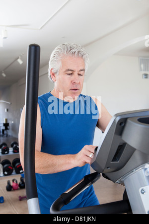 Older Hispanic man using elliptical machine in gym Stock Photo