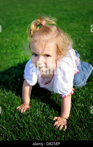 Cute little girl crawling on the green grass in the park Stock Photo