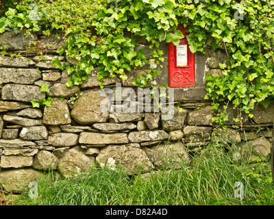 Red post box inside of dry stone wall inn a village at Stonewaite in Lake District, Cumbria, UK Stock Photo