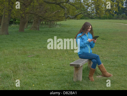 Young woman using iPad on bench in park. Stock Photo